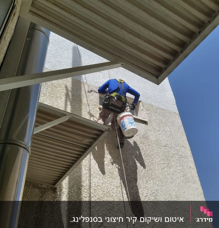 אדם תלוי על חבלים צובע קיר חיצוני